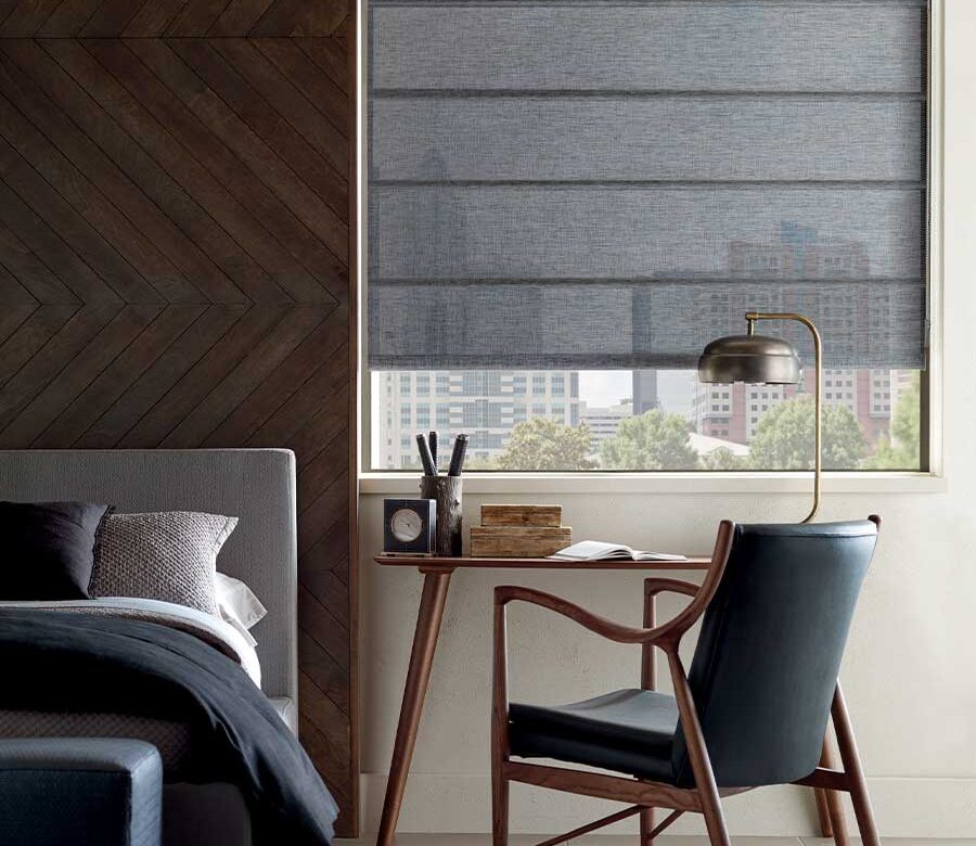 bed next to desk with charcoal architectural roller shades lowered, but still open