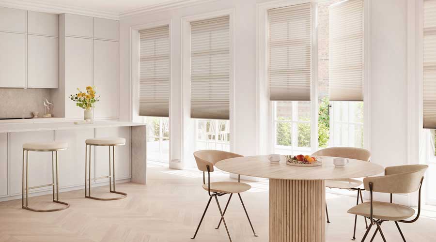 Duette® Honeycomb Shades covering floor to ceiling windows in a neutral kitchen. To the right of the photo is two chairs and a modern circular table