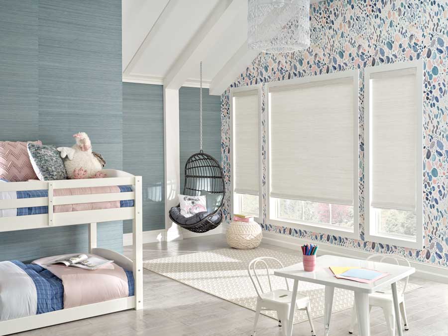 Provenance® Woven Woods in a bedroom with white bunk beds, pink bedspreads and a solid blue wall opposite of a blue and pink wallpaper wall that has three windows
