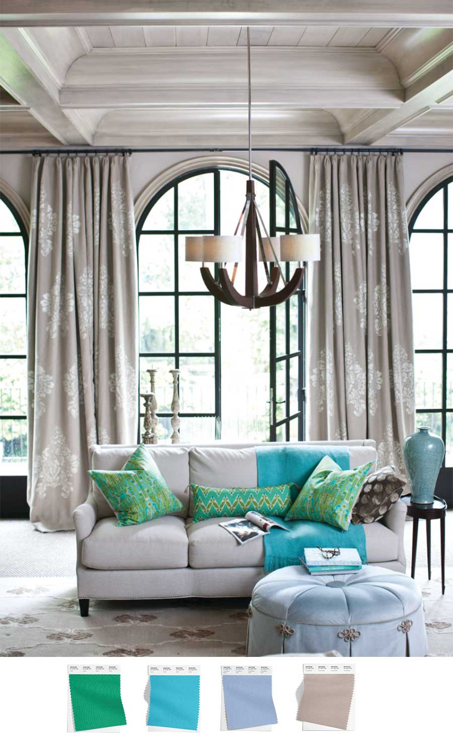 A living room with arched black trim doors that have fabric curtains hanging down on either side. The drapes are in a neutral color while blue and green pillows and blankets adorn the couch that is positioned in front of the window.