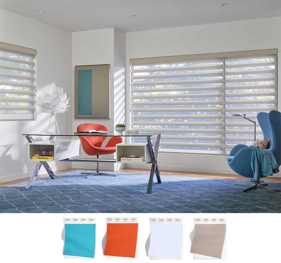 A corner office in a home with a blue rug, neutral walls, floor to ceiling wide windows with modern decor that has pops of color (orange and blue and white and tan). The windows are covered by pirouette shades.