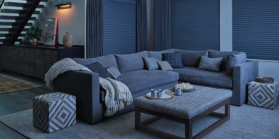 A dark living room with a sectional and coffee table. During the nighttime, the window coverings are closed providing great privacy