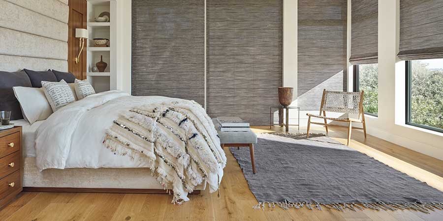 A neutral bedroom with alustra woven texture shades cascaded on two walls of windows in a neurtal bedroom