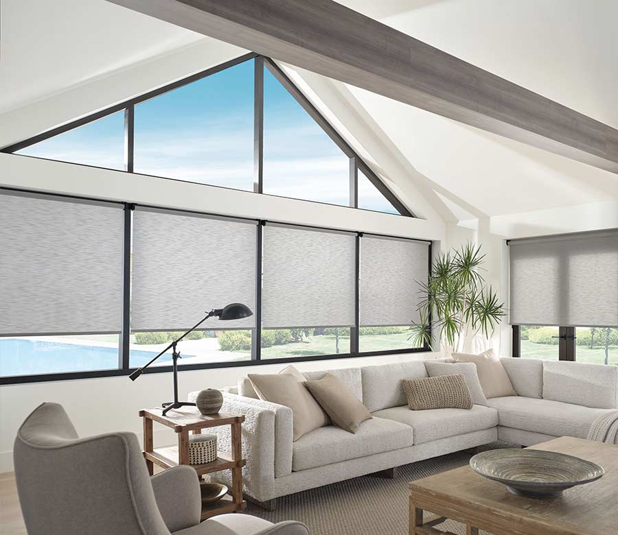 angled windows with gray shades in lofted ceiling family room with neutral couch and accents
