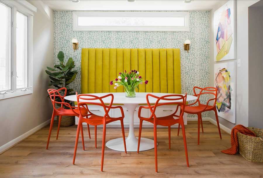 mustard yellow upholstered bench and dark orange chairs surround white table in dining space